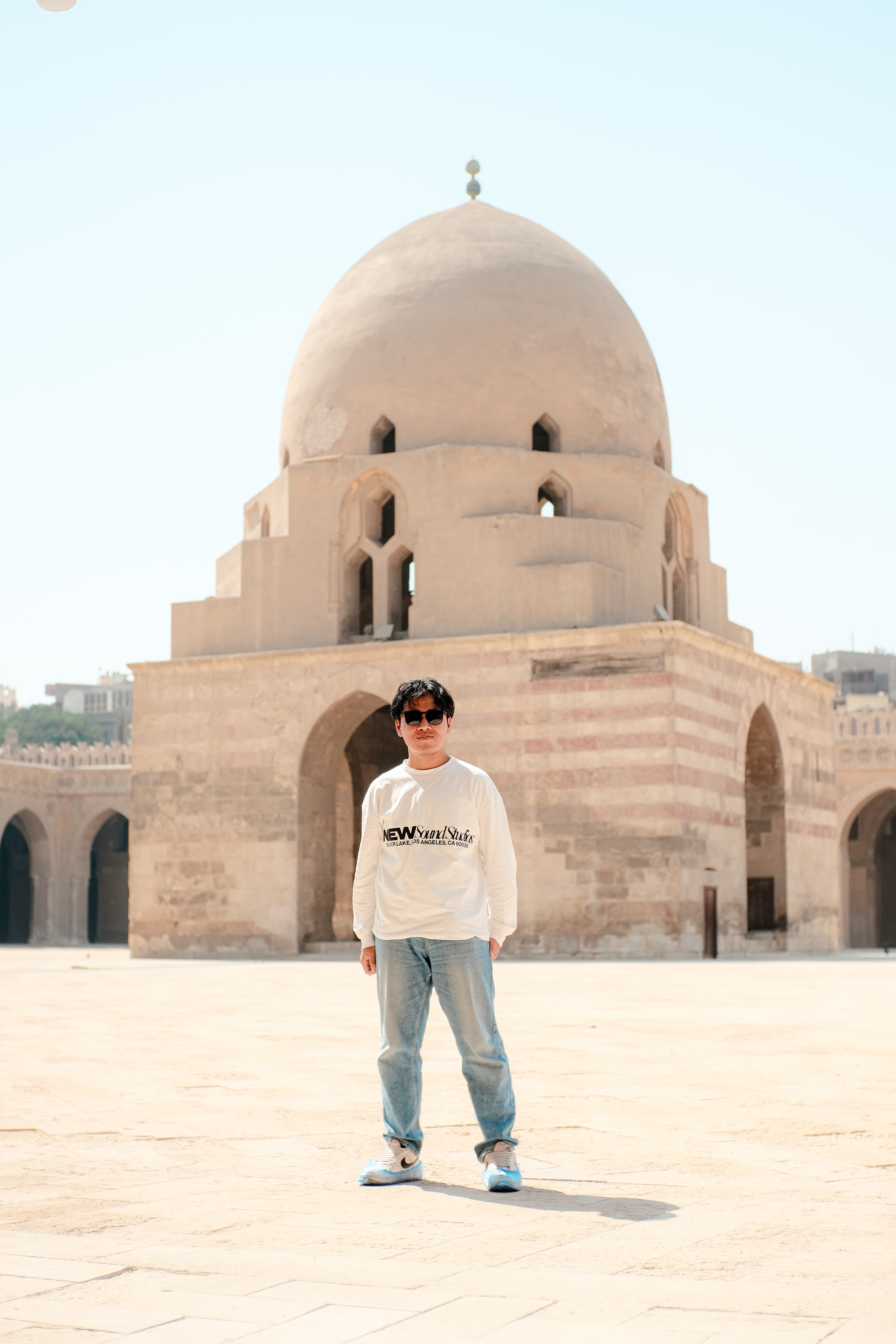 Fideligo wearing sunglasses and a cream shirt in front of historic sand-colored architecture